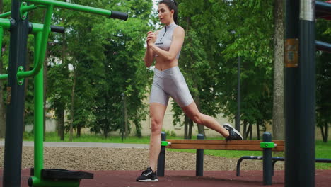 A-young-woman-in-a-Park-performs-lunges-squats-on-one-leg-on-a-bench-in-sportswear-in-the-summer.-Athletics-Caucasian-woman-trains-in-the-Park